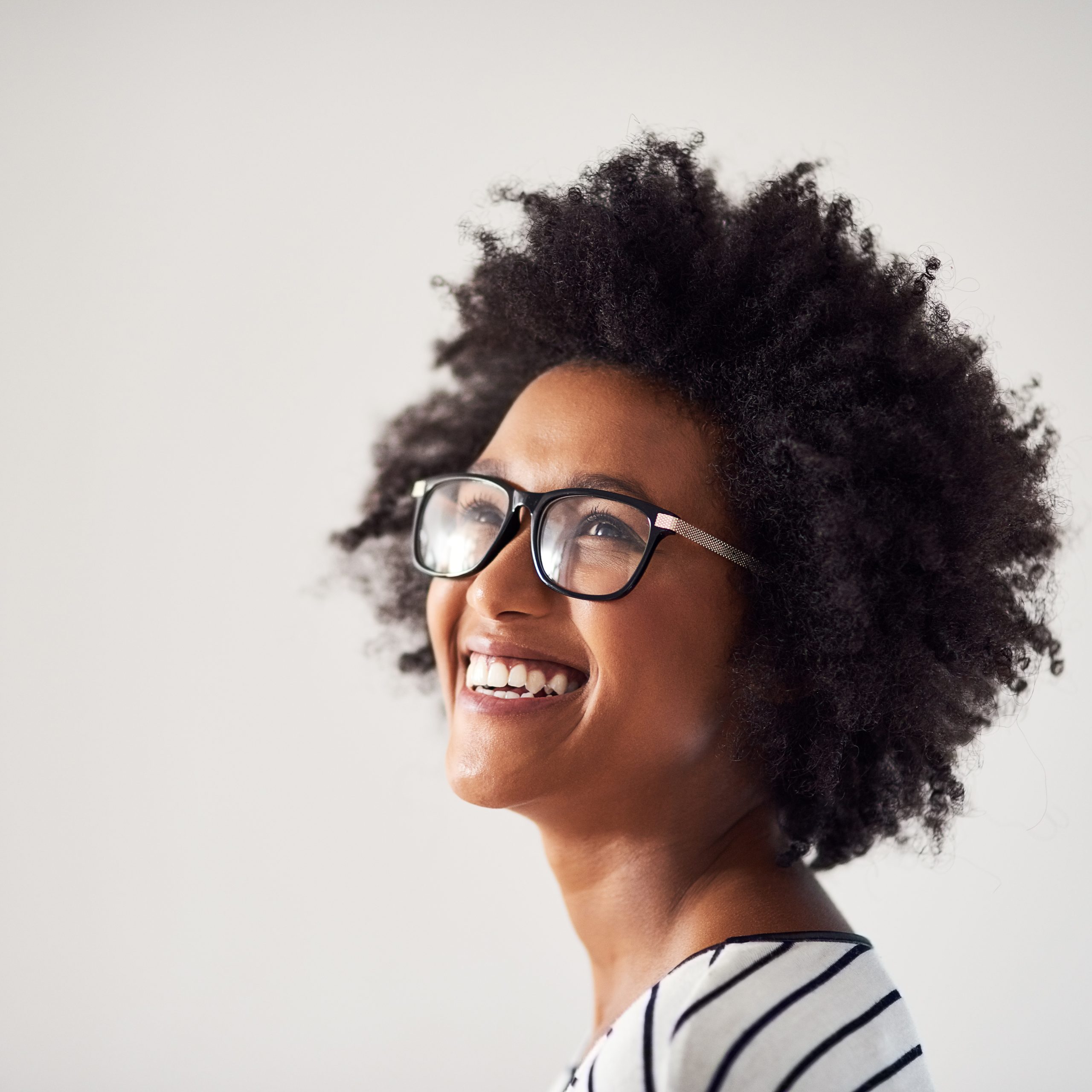 Studio shot of an attractive and happy young woman wearing glasses against a gray background.